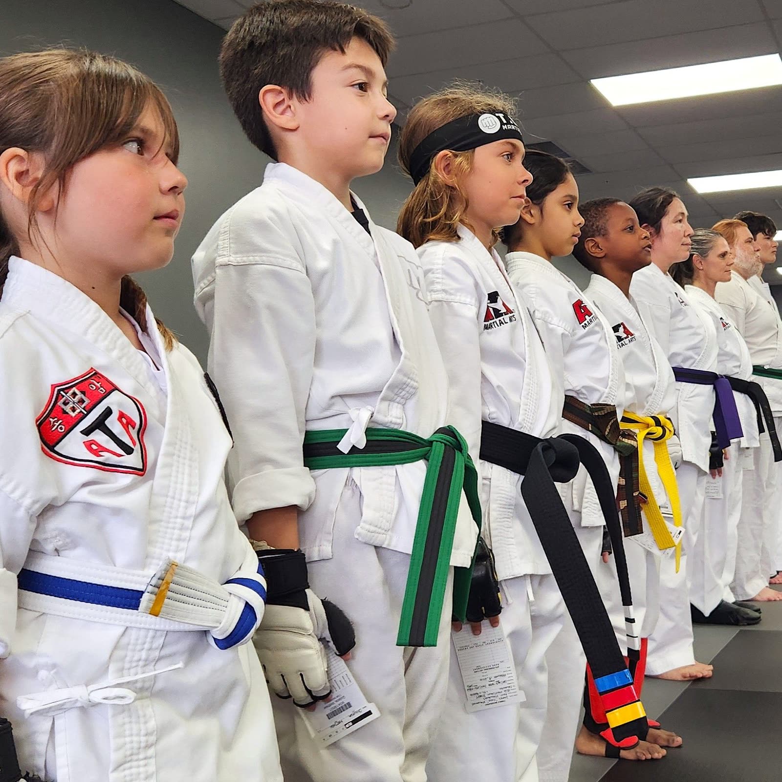Young students in white uniforms with colored belts lined up on the mat