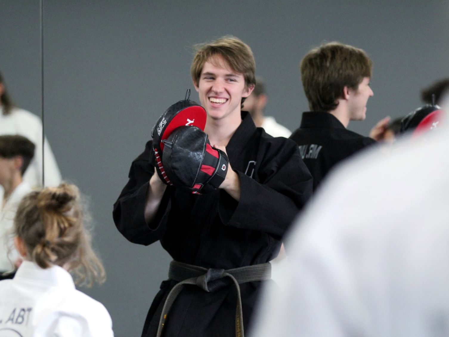 An instructor in a black uniform smiling while holding striking pads